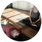 Två personer sitter på yogamattor i en sal och utövar långsamma rörelser